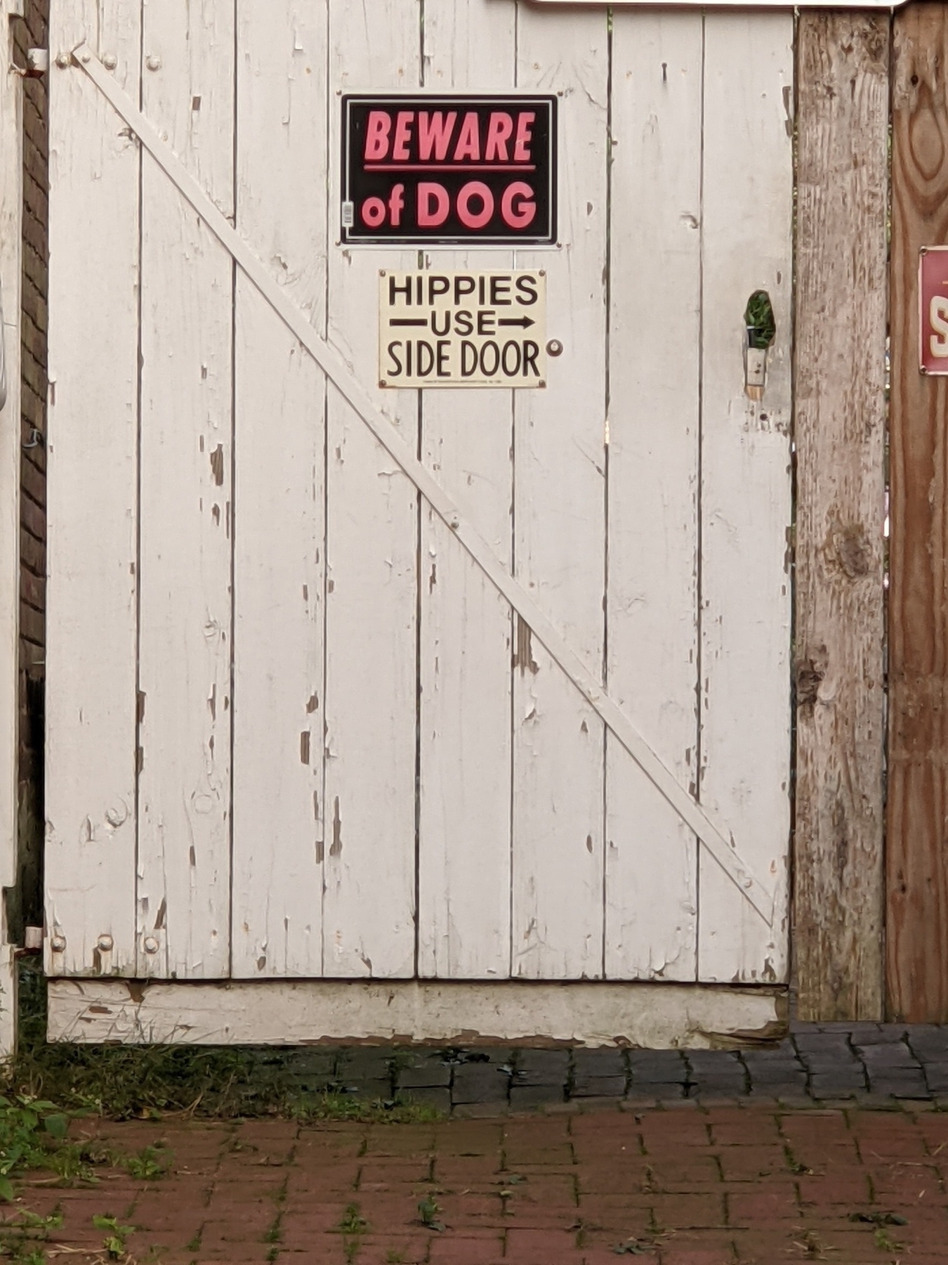 a vintage sign on a weatherbeaten gate reads hippies use side door
