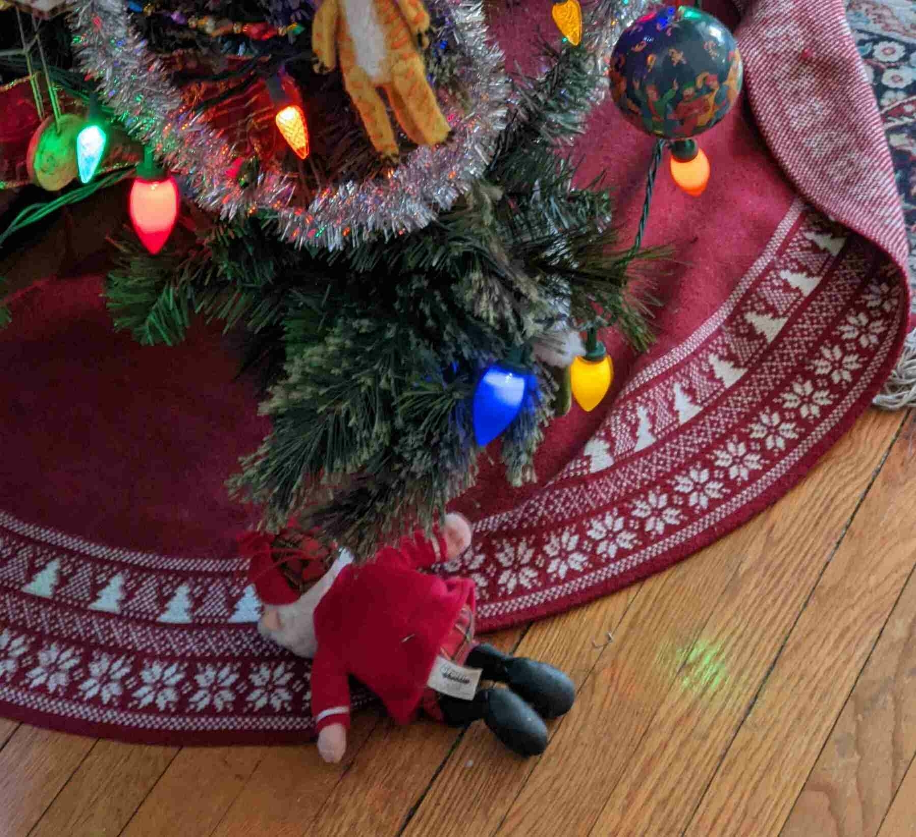 a Christmas tree ornament of Santa Claus is lying face-down on the floor, underneath a Christmas tree branch